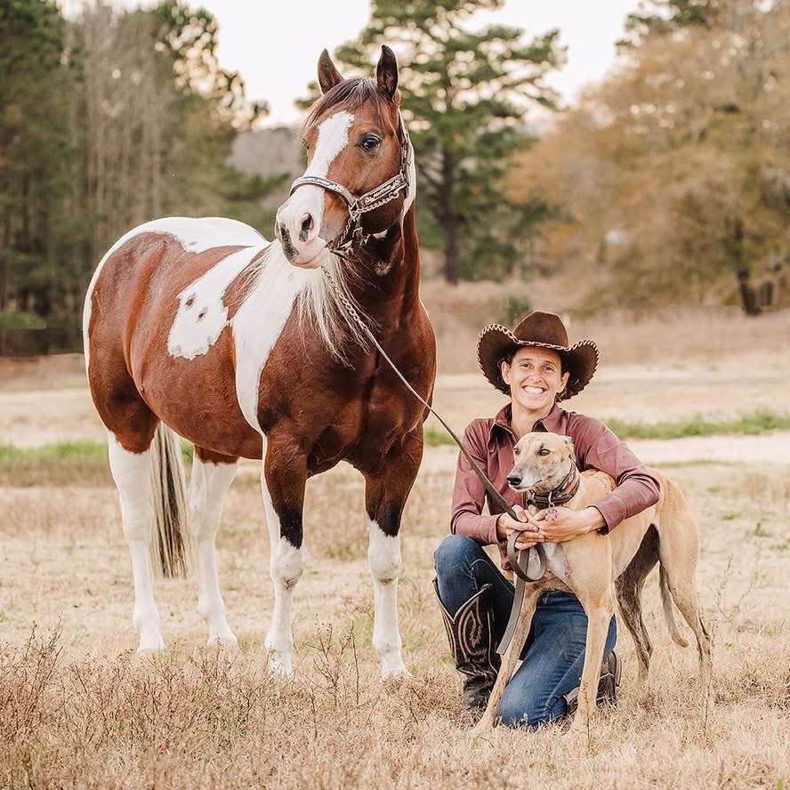 Trainer Tania Morton in a cowboy hat kneeling in a field with a paint horse and a greyhound on lead